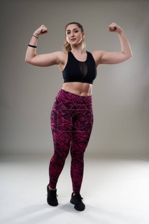 Foto de Mujer hispana joven más tamaño posando en traje de fitness sobre fondo gris - aceptación e inclusión - Imagen libre de derechos