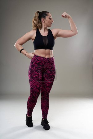 Foto de Mujer hispana joven más tamaño posando en traje de fitness sobre fondo gris - aceptación e inclusión - Imagen libre de derechos