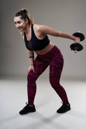Photo for Attractive plus size woman working out with dumbbells, isolated on gray background - Royalty Free Image