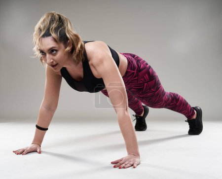 Téléchargez les photos : Plus la taille jeune femme faisant des exercices de fitness isométrique sur fond gris - en image libre de droit