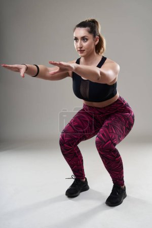 Photo for Plus size young woman doing isometric fitness exercises on gray background - Royalty Free Image
