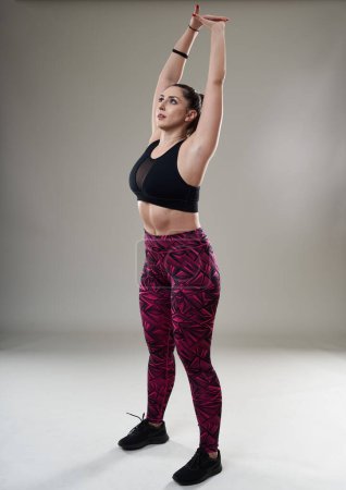 Photo for Confident plus size woman warming up and stretching before her workout, isolated on gray background - Royalty Free Image