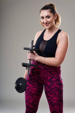 Photo for Attractive plus size woman working out with dumbbells, isolated on gray background - Royalty Free Image