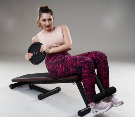 Téléchargez les photos : Confiant forte femme taille plus faire abdos croque sur un banc de fitness - en image libre de droit