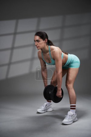 Foto de Mujer joven atlética en sujetador deportivo y pantalones cortos haciendo ejercicio fila de mancuerna sin el banco - Imagen libre de derechos