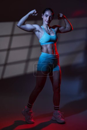 Téléchargez les photos : Modèle sportif de fitness jeune femme avec un corps parfait posant dans une lumière tonifiante bleu rouge dramatique avec projection de fenêtre sur fond, travail en studio - en image libre de droit