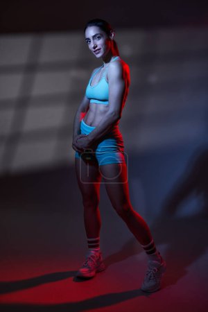 Téléchargez les photos : Modèle sportif de fitness jeune femme avec un corps parfait posant dans une lumière tonifiante bleu rouge dramatique avec projection de fenêtre sur fond, travail en studio - en image libre de droit