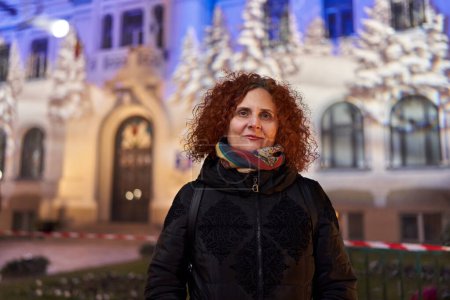 Téléchargez les photos : Curly haired redhead woman at night in the city with festive lights, closeup environmental portrait - en image libre de droit