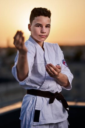 Photo for Young teenage boy karate practitioner in white kimono training on the roof top at sunset - Royalty Free Image