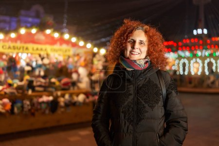 Téléchargez les photos : Curly haired redhead woman at night in the city with festive lights, closeup environmental portrait - en image libre de droit