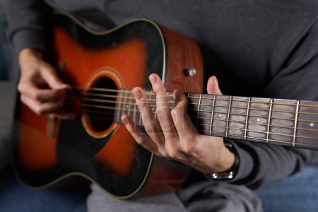 Foto de Young man playing an acoustic guitar on the sofa in the living room - Imagen libre de derechos