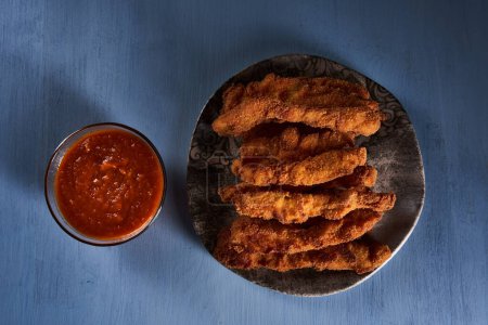 Foto de Chicken strips, croquettes with salsa sauce and nacho chips on a blue wooden board - Imagen libre de derechos