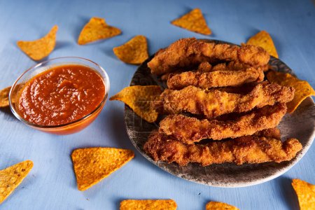 Téléchargez les photos : Chicken strips, croquettes with salsa sauce and nacho chips on a blue wooden board - en image libre de droit