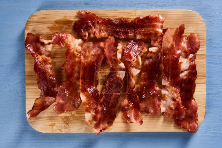 Photo for Strips of matured bacon fried and served on a wooden board - Royalty Free Image