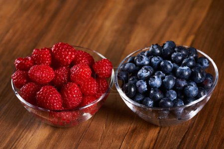 Photo for Raspberries and blueberries in bowls on a wooden board - Royalty Free Image