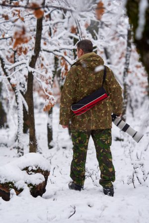 Foto de Fotógrafo profesional de vida silvestre en un bosque de robles nevados con su teleobjetivo en cámara - Imagen libre de derechos
