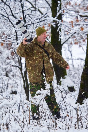 Téléchargez les photos : Professional wildlife photographer in a snowy oak forest with his telephoto lens on camera - en image libre de droit