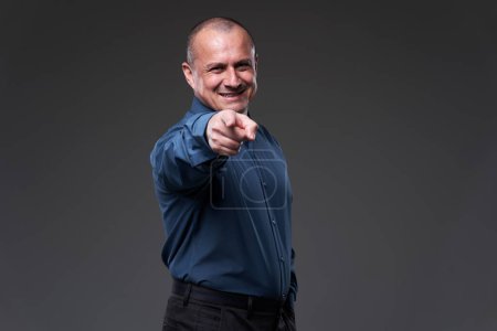 Téléchargez les photos : Smiling businessman pointing at the camera, as if choosing the viewer amongst everyone else on gray background - en image libre de droit
