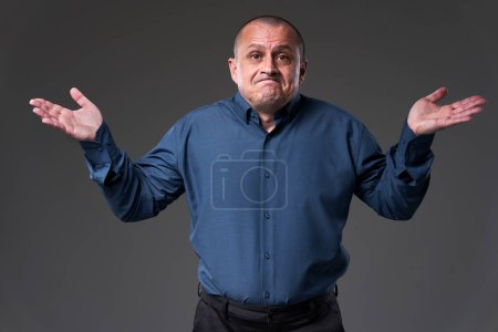 Foto de Powerless mature businessman with arms raised with an I can't do anything expression on his face, gray background - Imagen libre de derechos
