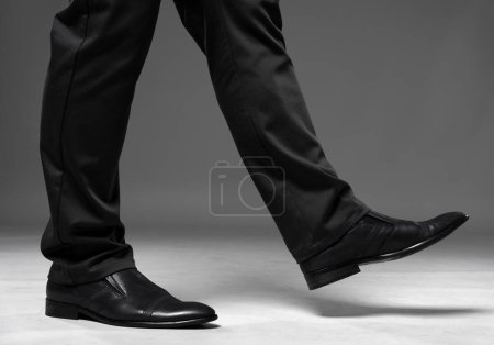 Foto de Legs of a man walking in elegant black trousers and leather shoes on gray background - Imagen libre de derechos