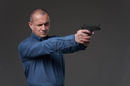 Foto de Mature businessman with a gun taking aim at the competition, gray background - Imagen libre de derechos
