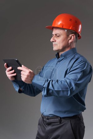 Photo for Engineer in hardhat doing planning digitally with a tablet, gray background - Royalty Free Image