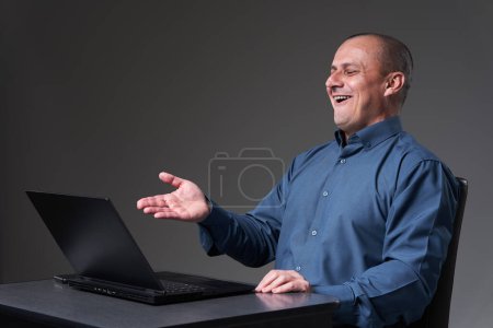 Téléchargez les photos : Homme d'affaires mature assis à son bureau travaillant sur ordinateur portable, sur fond gris - en image libre de droit