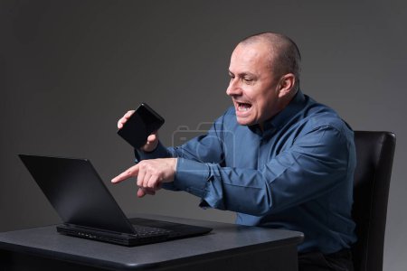 Photo for Very angry and demanding mature businessman yelling in a phone conference, while being at his laptop - Royalty Free Image
