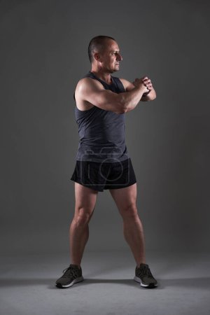 Foto de Foto de cuerpo completo de un hombre maduro haciendo un entrenamiento de fitness sobre fondo gris - Imagen libre de derechos