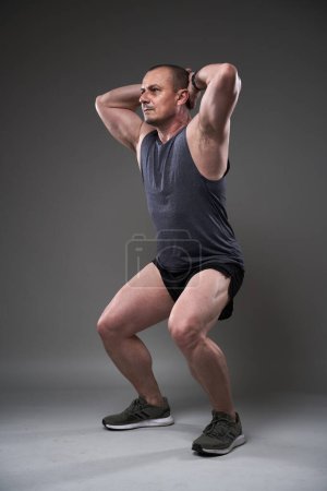 Photo for Mature caucasian muscular man in tee and shorts doing a fitness workout training on gray background - Royalty Free Image