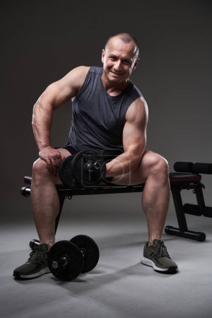 Téléchargez les photos : Mature caucasien musclé homme en tee et shorts faire un entraînement de remise en forme sur fond gris - en image libre de droit