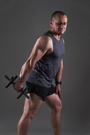 Photo for Mature caucasian muscular man in tee and shorts doing a fitness workout training on gray background - Royalty Free Image