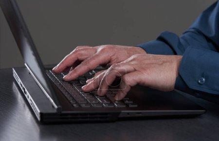 Photo for Hands of a mature businessman typing on his laptop, closeup shot on gray - Royalty Free Image