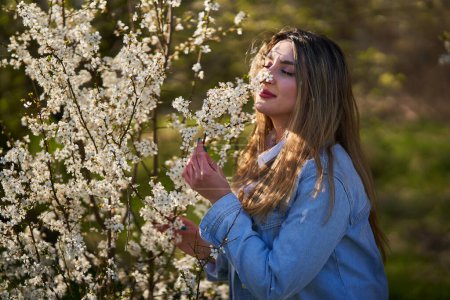 Photo for East asian young woman enjoying spring in a park with flowering trees - Royalty Free Image