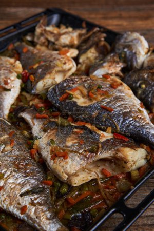 Photo for Delicious oven cooked bream in a metal tray on rustic wooden board - Royalty Free Image