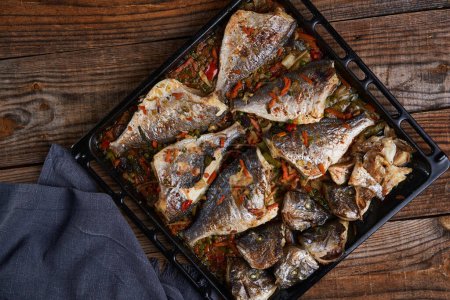 Photo for Delicious oven cooked bream in a metal tray on rustic wooden board - Royalty Free Image