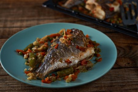 Photo for Grilled bream with vegetables on a blue plate on a wooden board - Royalty Free Image