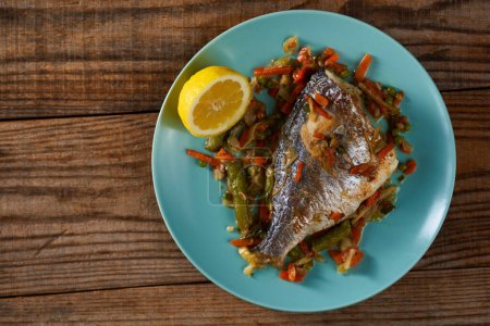 Photo for Grilled bream with vegetables on a blue plate on a wooden board - Royalty Free Image