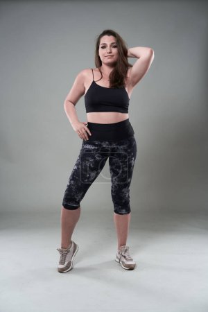 Photo for Attractive plus size woman in fitness top and tights, gray background - Royalty Free Image
