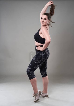 Photo for Attractive plus size woman in fitness top and tights, gray background - Royalty Free Image