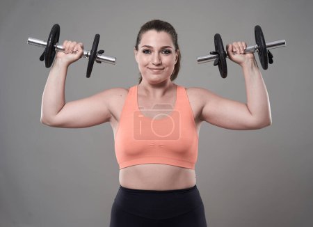 Foto de Fuerte confianza más tamaño mujer joven ejercitando ejercicios de fitness con pesas - Imagen libre de derechos