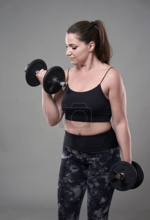Foto de Fuerte confianza más tamaño mujer joven ejercitando ejercicios de fitness con pesas - Imagen libre de derechos