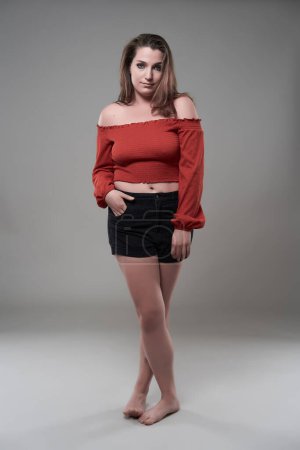 Téléchargez les photos : Portrait studio d'une jeune femme confiante plus la taille sur fond gris - en image libre de droit