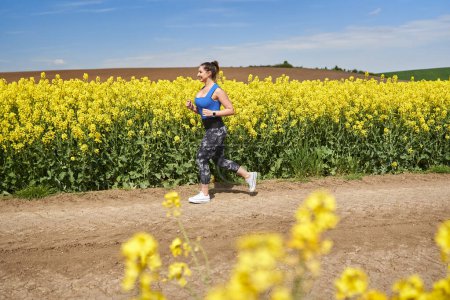 Photo for Plus size beautiful latin woman jogging on a dirt road by a canola field - Royalty Free Image