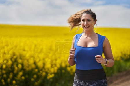Foto de Más tamaño hermosa mujer latina corriendo en un camino de tierra por un campo de canola - Imagen libre de derechos