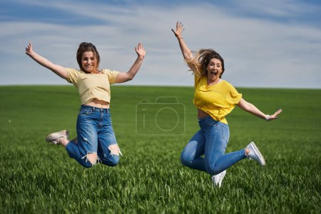 Foto de Dos chicas grandes saltando de alegría y divirtiéndose en un campo de trigo - Imagen libre de derechos