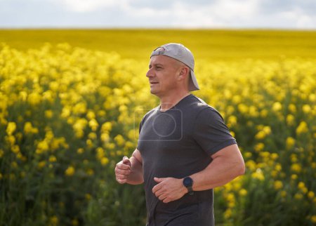 Photo for Middle aged distance runner running on a dirt road in a blooming canola field - Royalty Free Image