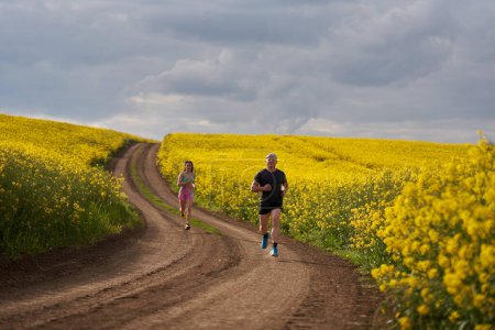 Téléchargez les photos : Deux coureurs qui courent sur un parcours vallonné sur une piste de terre dans un champ de canola - en image libre de droit