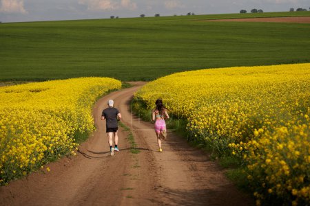 Photo for A couple of runners running on a hilly course on a dirt track in a canola field - Royalty Free Image