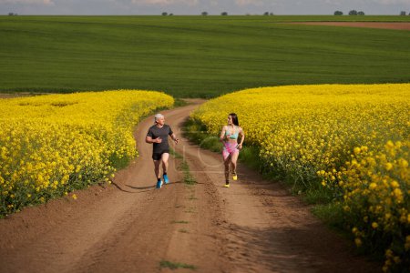 Foto de Un par de corredores corriendo en un curso montañoso en una pista de tierra en un campo de canola - Imagen libre de derechos
